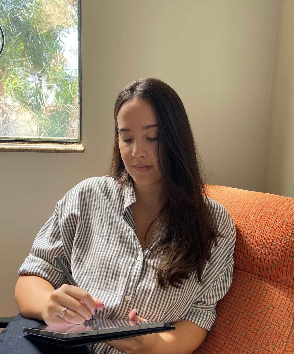 Laura Alcântara fazendo anotações em um tablet perto da janela